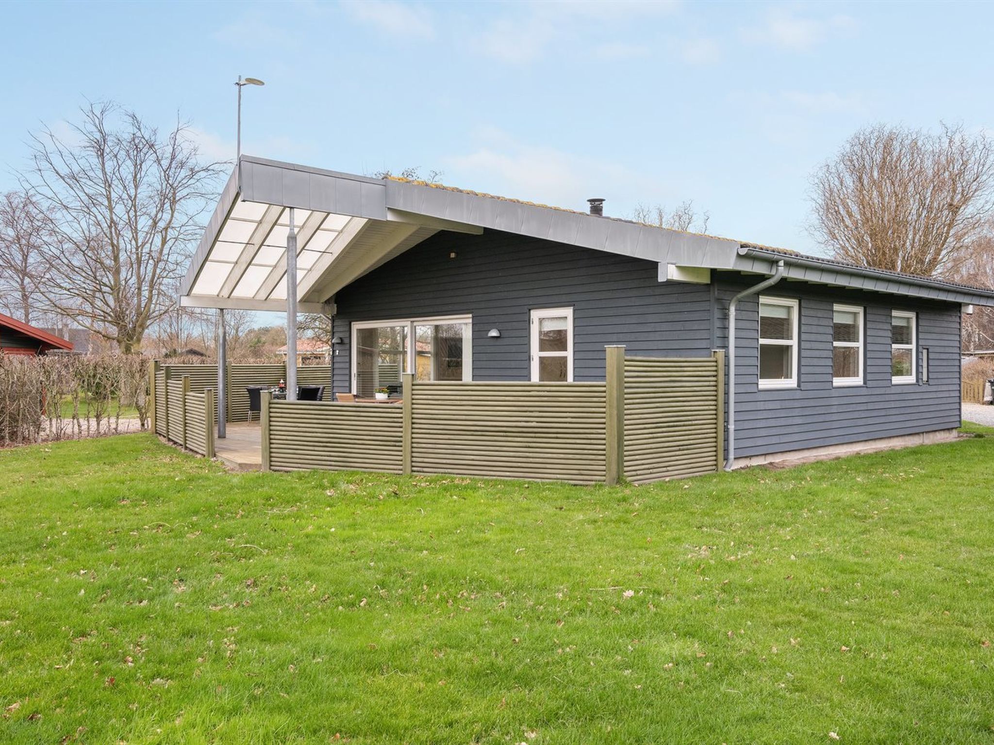 Une maison moderne dotée d’un patio couvert, d’une cour clôturée et offrant une vue sur un ciel dégagé.