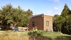 A small wooden cabin with a door and windows, surrounded by trees and a grassy area.