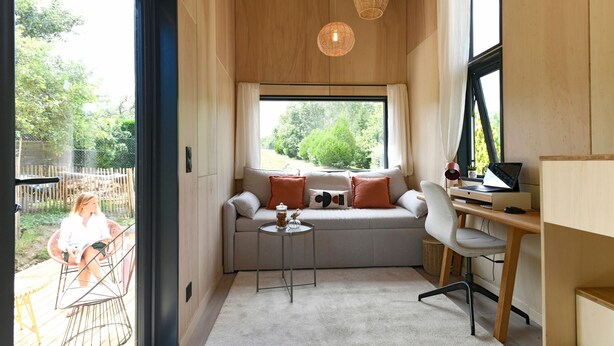 A modern interior with a sofa, a small table, a desk, and a large window.