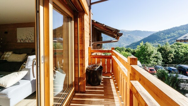 Un balcón de madera con vistas a montañas, un sofá y un cubo de basura.