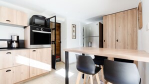 Una cocina moderna con una mesa de madera, sillas negras, electrodomésticos de acero inoxidable y armarios de madera.
