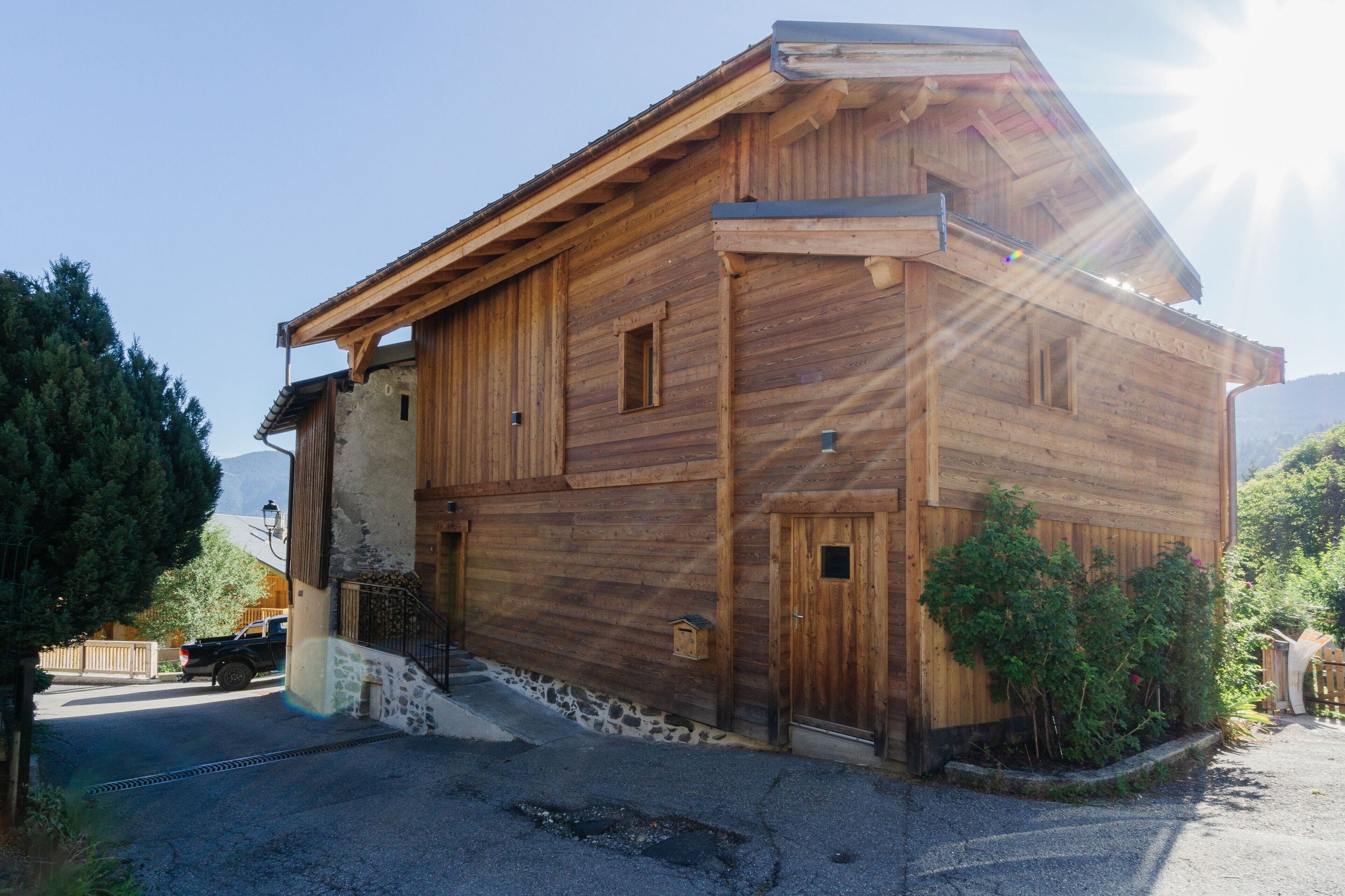 Un bâtiment en bois avec un toit en pente, un escalier menant à l’entrée et un véhicule garé à l’extérieur.