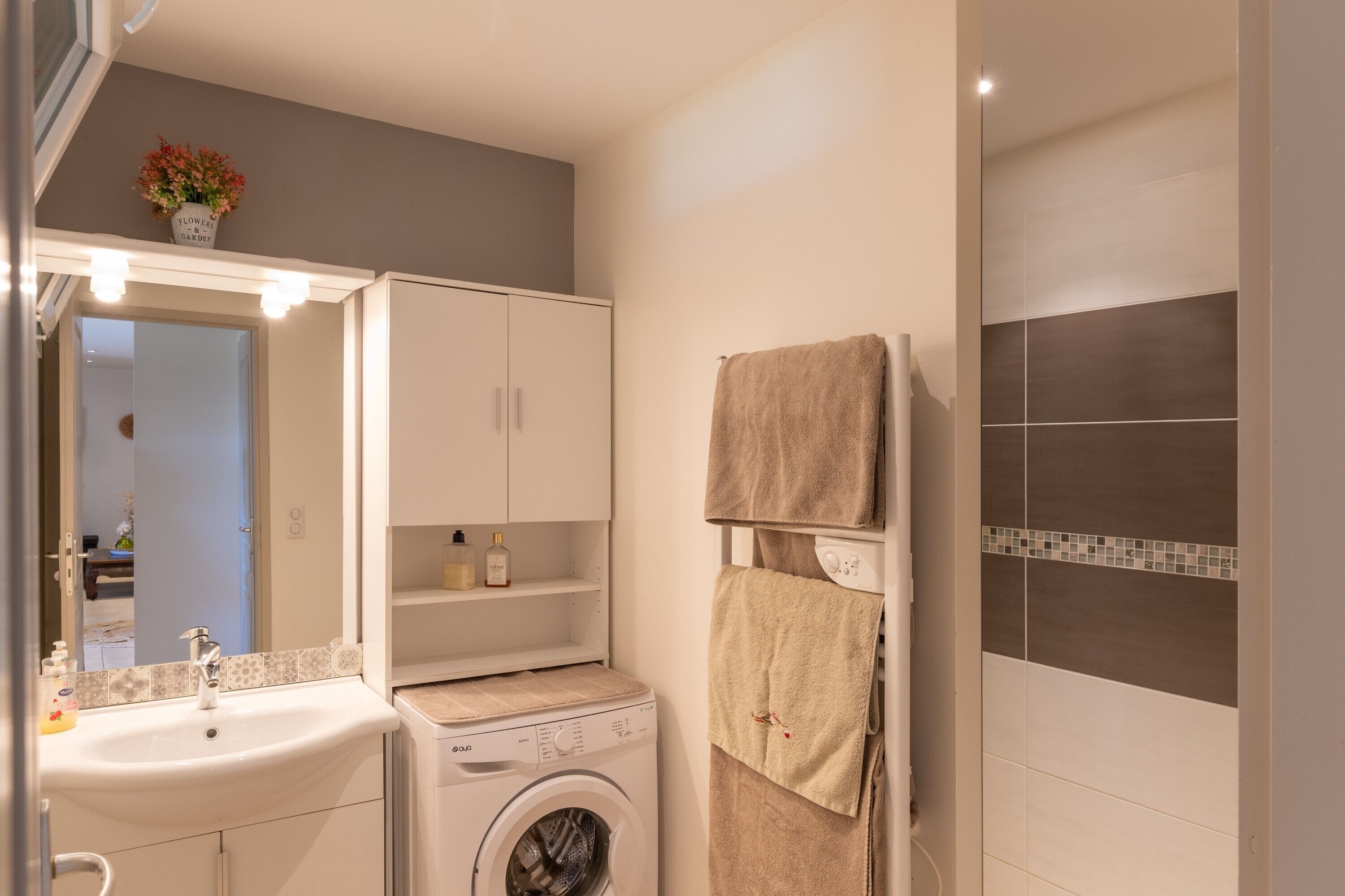 Een badkamer met een wastafel, spiegel, kastje, handdoekhouder en een wasmachine.