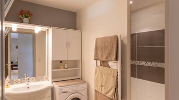 Een badkamer met een wastafel, spiegel, kastje, handdoekhouder en een wasmachine.