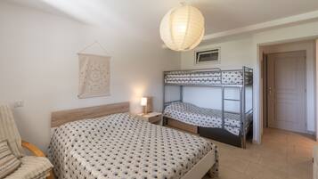 Une chambre avec des lits superposés, une chaise, une table de chevet avec une lampe, une décoration murale et une porte.