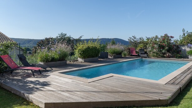 Ein rechteckiger Pool mit Holzterrasse, umgeben von üppigem Grün und blauem Himmel.