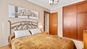 Une chambre à coucher comprenant un lit, une table de chevet, une lampe, une armoire en bois et une œuvre d’art accrochée au mur.