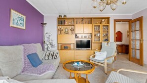Un salon comprenant un canapé, un fauteuil, un téléviseur, des étagères en bois et un lustre.