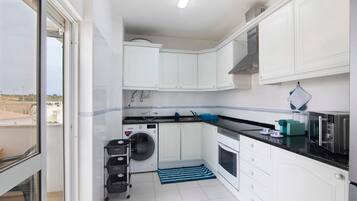 Una cocina compacta con armarios blancos, lavadora, microondas y tostadora.