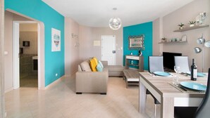 Ein modernes Wohnzimmer mit einer Couch, einem Esstisch für zwei Personen und einer sichtbaren Küche im Hintergrund.