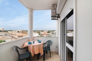 Un balcon avec une table et des chaises, une vue sur les immeubles et une fenêtre avec des stores.