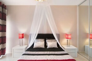 Quarto com cama, mesas de cabeceira brancas, luminárias vermelhas, cama com dossel e espelho.