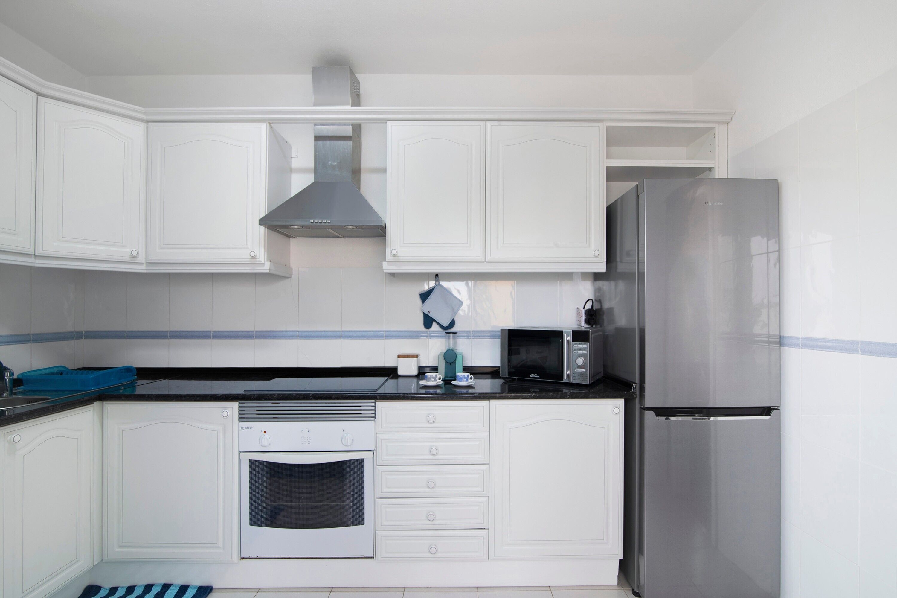 Una cocina con armarios blancos, un refrigerador de acero inoxidable, un microondas y un horno.