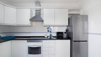 Una cocina con armarios blancos, un refrigerador de acero inoxidable, un microondas y un horno.