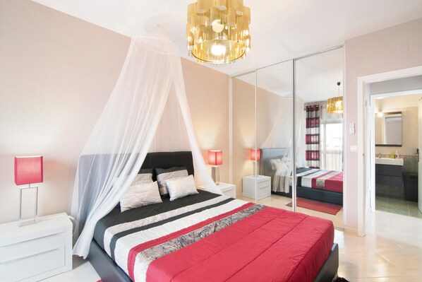 Une chambre à coucher avec un lit, des tables de chevet, un miroir et un lustre.