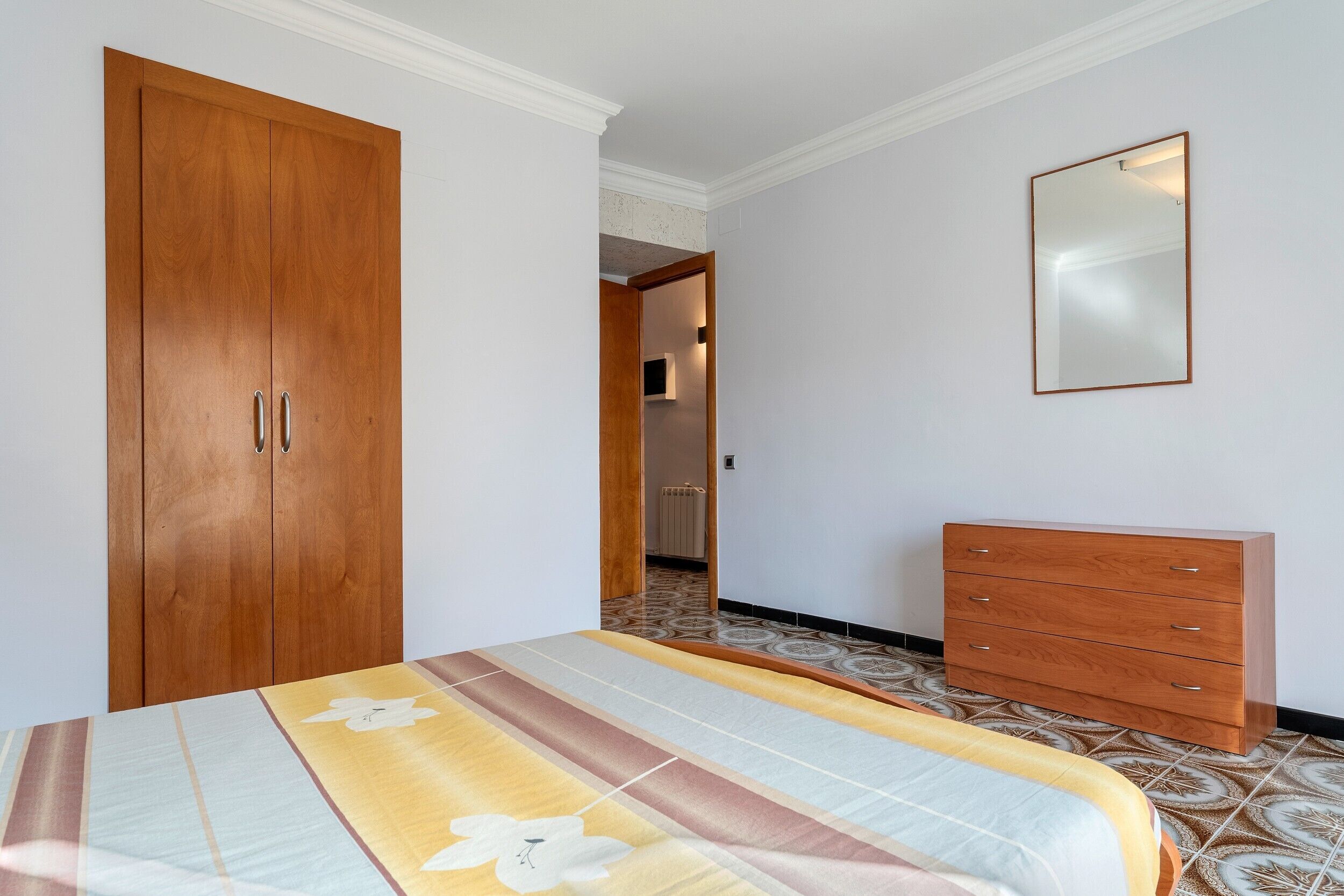 Een slaapkamer met een bed, een kledingkast, een dressoir en een spiegel.