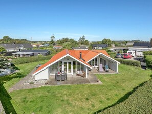 Une maison moderne avec un toit rouge, un patio couvert et une pelouse bien entretenue.