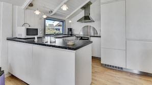 Cocina moderna con armarios blancos, encimera negra, microondas, cafetera y un amplio ventanal con vistas al exterior.