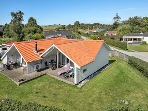 Une maison moderne avec un toit rouge, un patio couvert et une pelouse bien entretenue.