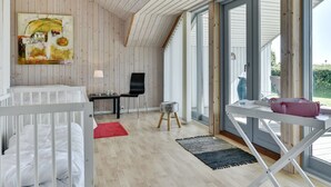 Una habitación moderna y bien iluminada, con techo inclinado, paredes de madera, un ventanal grande, una cama, un escritorio y una silla.