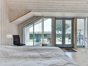 Une chambre avec un grand lit, une chaise et une vue sur un patio aménagé avec du mobilier d’extérieur.