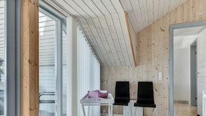Una habitación con techo inclinado, paredes de madera, un ventanal grande y una mesa con sillas.