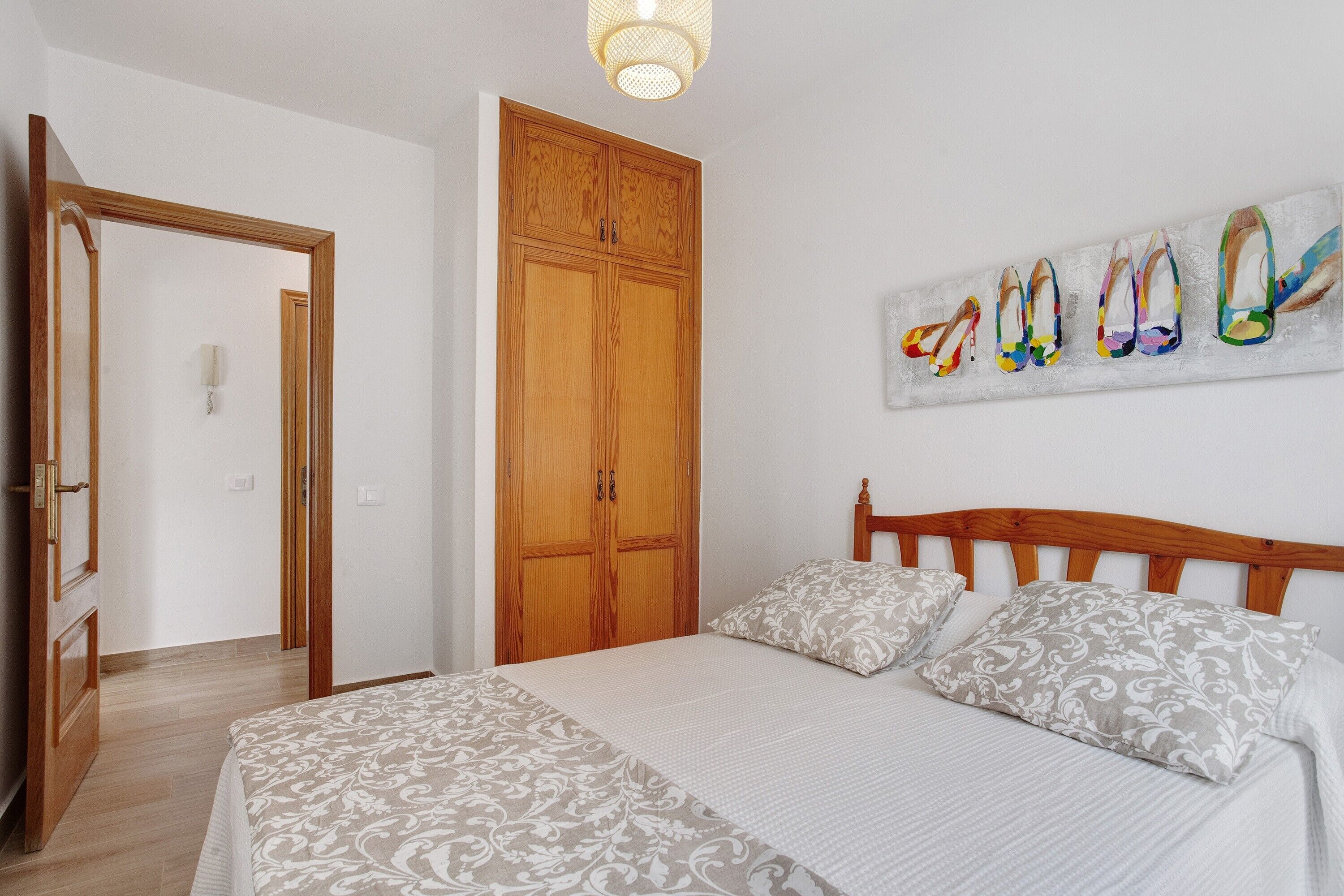 A bedroom with a bed, wooden wardrobe, and a wall-mounted shoe art piece.
