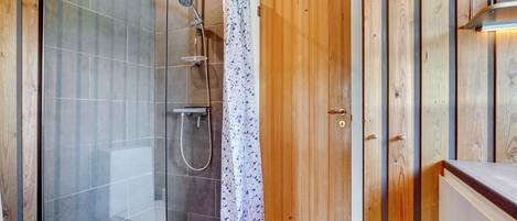 Een moderne badkamer met een douchecabine van glas, een houten deur en een witte wastafel.