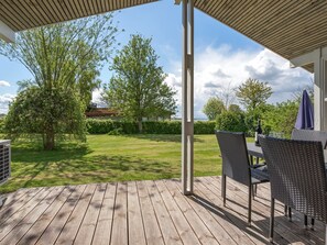 En træterrasse med udendørs møbler, udsigt til en græsplæne og træer.