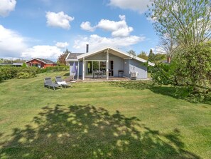 Et moderne hus med en overdækket terrasse, græsplæne og swimmingpool.