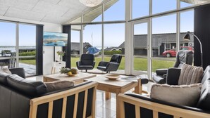 A spacious living room with large windows, a modern chandelier, and a view of the outside.
