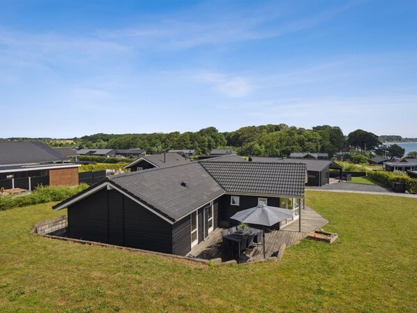 A modern residential area with houses featuring dark roofs and wooden exteriors, surrounded by greenery and a clear sky.
