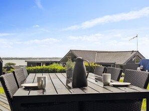 A wooden table with two white cups and a black pitcher, set on a deck with wicker chairs.