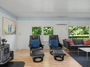 A room with two reclining chairs, a sofa, a table, a fireplace, and large windows with a view of greenery.