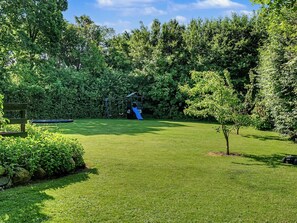 Une cour arrière verdoyante avec une balançoire et un toboggan, entourée d’arbres touffus.