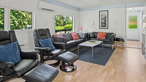 Un salon moderne avec des canapés en cuir, une table basse et de grandes fenêtres donnant sur un paysage verdoyant.