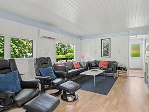 A modern living room with leather sofas, a coffee table, and large windows offering a view of greenery.