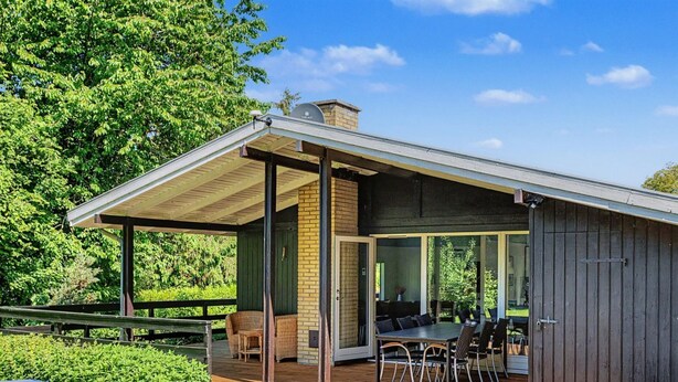 Une terrasse extérieure moderne, dotée d'une plateforme en bois, de meubles en osier et d'un espace repas fermé par des parois de verre.