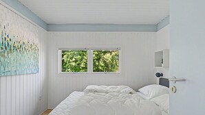 Une chambre à coucher avec un lit, deux fenêtres, un tableau et une porte avec une poignée.