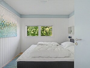 A bedroom with a bed, two windows, a painting, and a door with a handle.