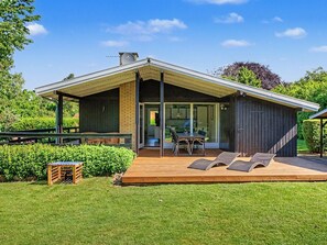 Et moderne hus med en træterrasse, et spiseområde med udendørs møbler og et stort vindue.