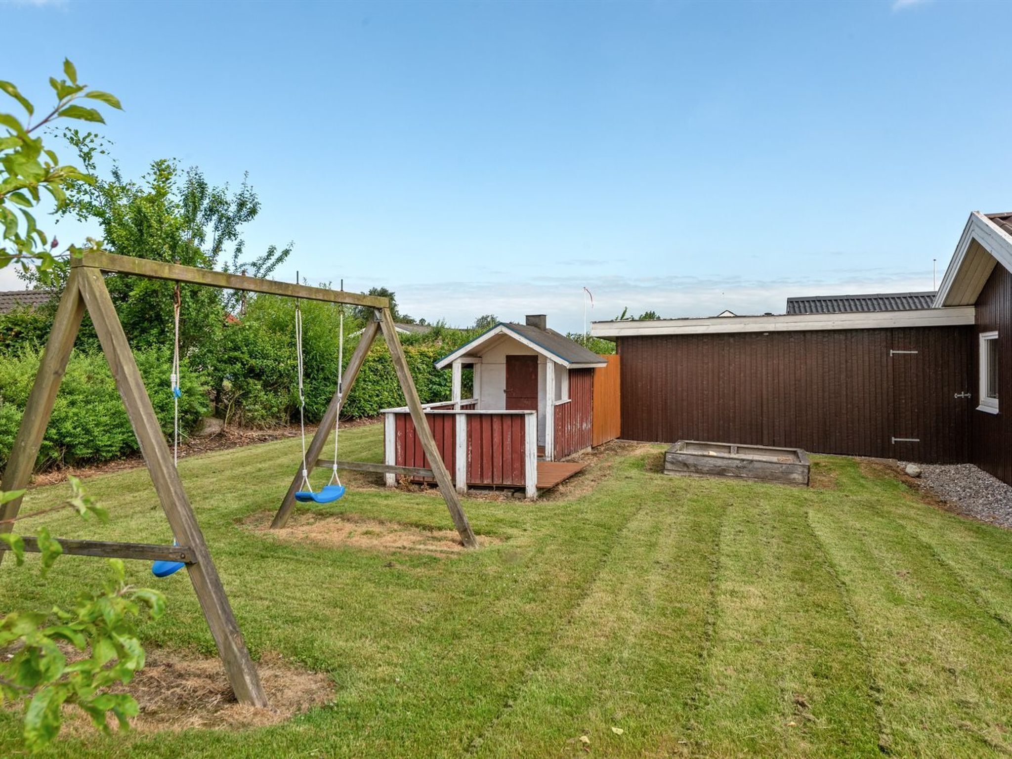 A backyard with a wooden swing set, a small shed, and a fenced area.