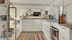 Una cocina moderna con armarios blancos, encimera de madera y una isla central. Hay una lámpara colgante sobre la isla y una estufa a la derecha.