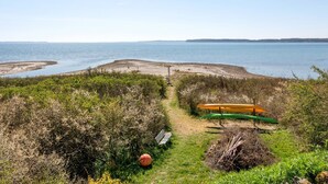 Un paisaje costero con vista despejada al mar, una playa de arena y un sendero que lleva a un kayak verde y naranja.