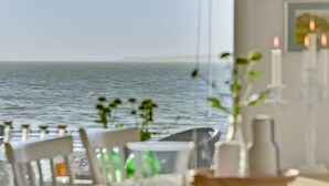 Un comedor con vistas al mar, con una mesa dispuesta con velas y un jarrón de flores.