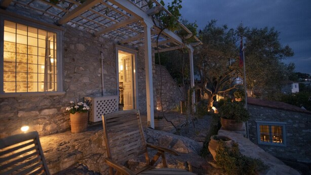 Un bâtiment en pierre avec une pergola en bois, une chaise en bois et une plante en pot.