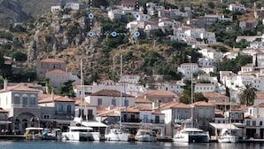 Une ville côtière aux bâtiments blancs, un port de plaisance avec des bateaux, et une colline en arrière-plan.