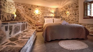 Une chambre aux murs de pierre, avec un lit, deux lampes fixées au mur, une table de chevet et une fenêtre.