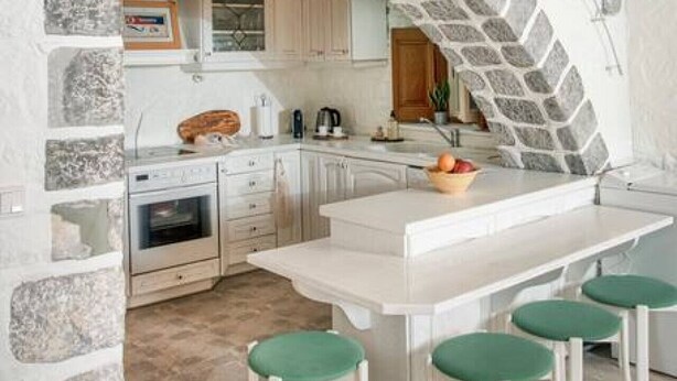 Une cuisine dotée d’une arche en pierre, de meubles blancs et d’un îlot central avec des tabourets verts.