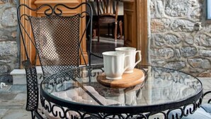 A glass table with a metal chair, a white mug, and a wooden coaster.